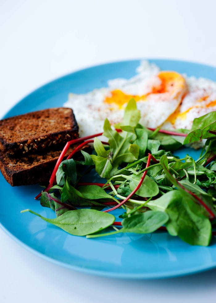 Close-up of a nutritious breakfast with eggs, green salad, and toast on a blue plate.