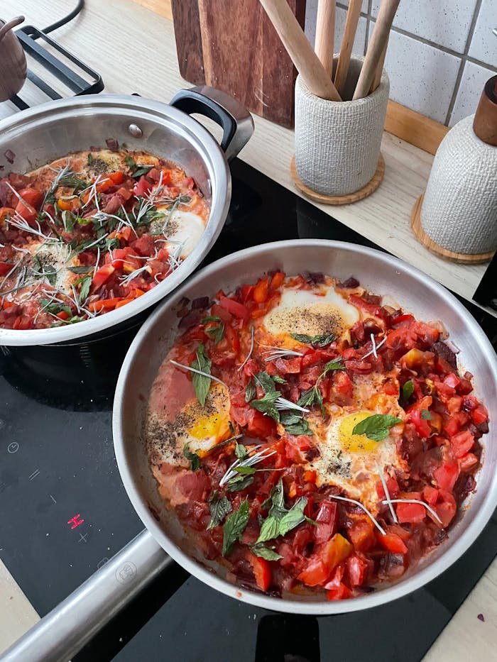 Savory shakshuka with eggs and herbs prepared in a stylish kitchen setup.